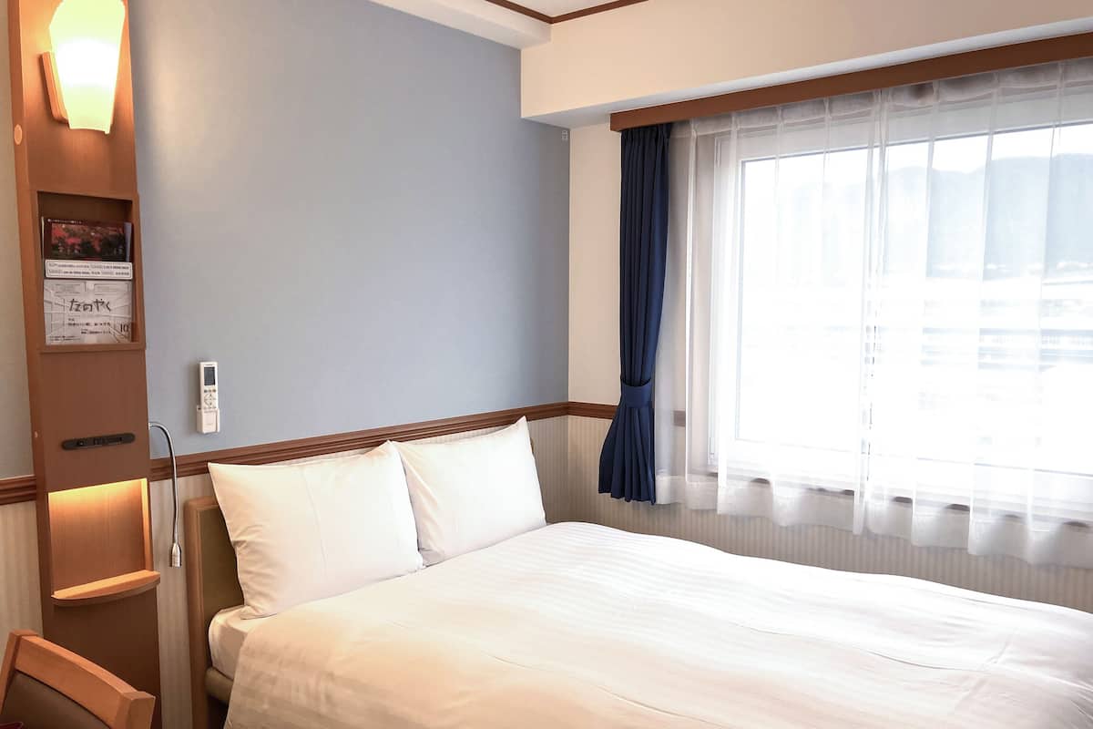 Een hotelkamer met een groot bed, een nachtkastje, een stoel, een aan de muur bevestigde televisie en een raam met gordijnen.