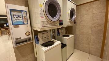 A laundry facility with stacked washing machines and dryers, a water dispenser, and a tiled floor.