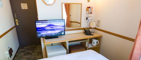 Une chambre d’hôtel équipée d’un lit, d’un bureau avec un écran d’ordinateur, d’un téléphone, d’une bouilloire et d’une horloge murale.