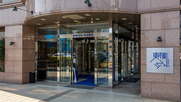 The entrance to a building with a glass door and a blue carpet leading inside. There is a sign above the door with Japanese text. - Toyoko Inn Kumamoto Ekimae (Kumamoto)