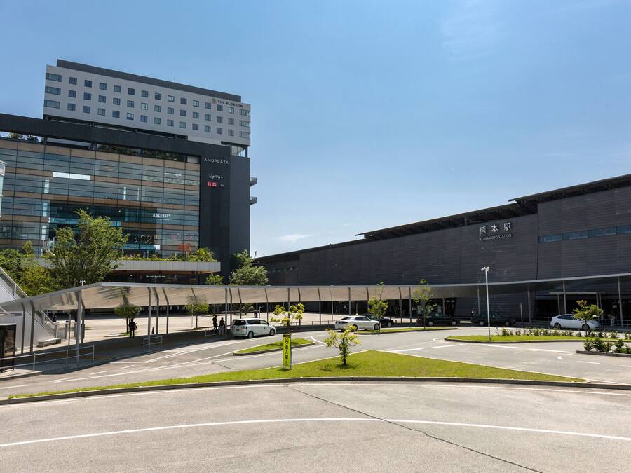 A modern building with multiple floors, a covered entrance area, and a parking lot with several cars.