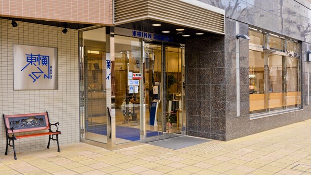 A building entrance with a tiled facade, a bench outside, and a glass door with signage. - Toyoko Inn Hamamatsu Station (Hamamatsu)