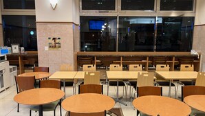 A restaurant with round tables and chairs, a kitchen area, and large windows. - Toyoko Inn Hamamatsu Station (Hamamatsu)