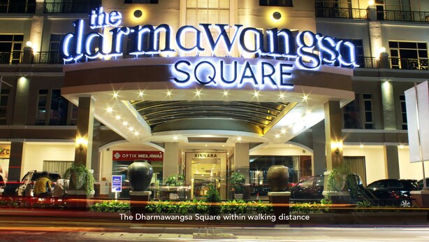Fachada del hotel Dharmowangs Square iluminada por la noche, con señalización luminosa y un diseño arquitectónico moderno.