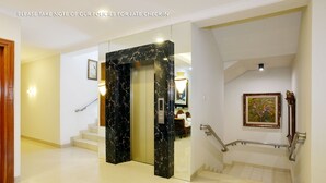 Un moderno vestíbulo de hotel con un ascensor de mármol, una escalera y una obra de arte enmarcada en la pared.