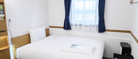 A hotel room with a bed, a window with curtains, a bedside table, and a chair.