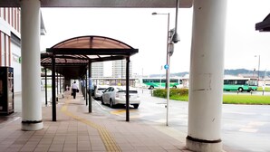 Un paso elevado cubierto para peatones con pavimento táctil, una parada de autobús y una fila de coches estacionados.