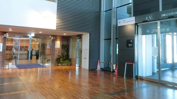 Un edificio moderno con fachada de vidrio, piso de madera y señalización que indica un segundo aula y un Toyoko Inn.