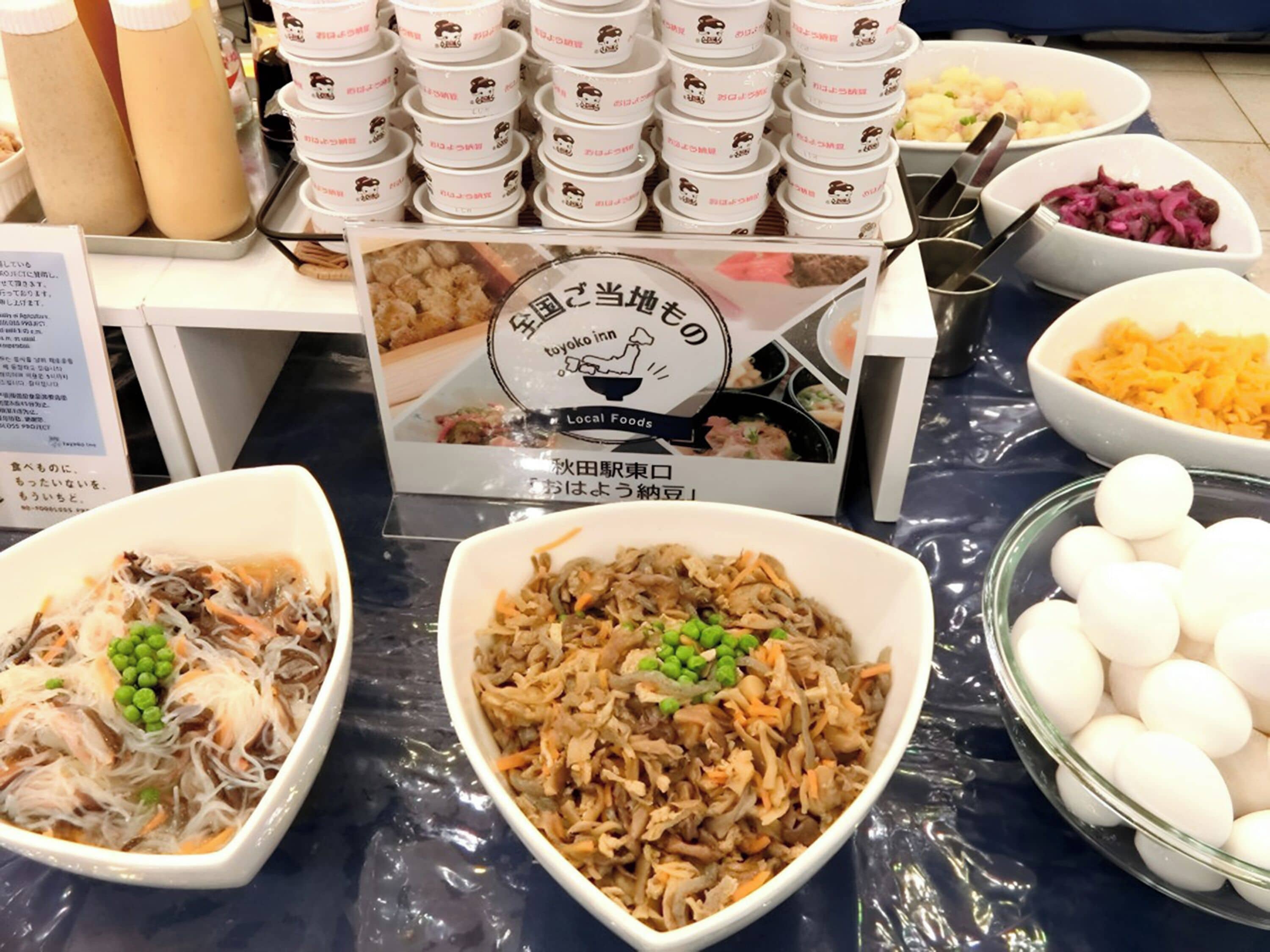 Una mesa de buffet con diversos platos, incluyendo un tazón de carne desmenuzada con guisantes, un tazón de esferas blancas y una presentación de recipientes pequeños con un logotipo.