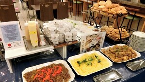 Un bufé con diversos platos, entre ellos fideos, brócoli y una variedad de panes.