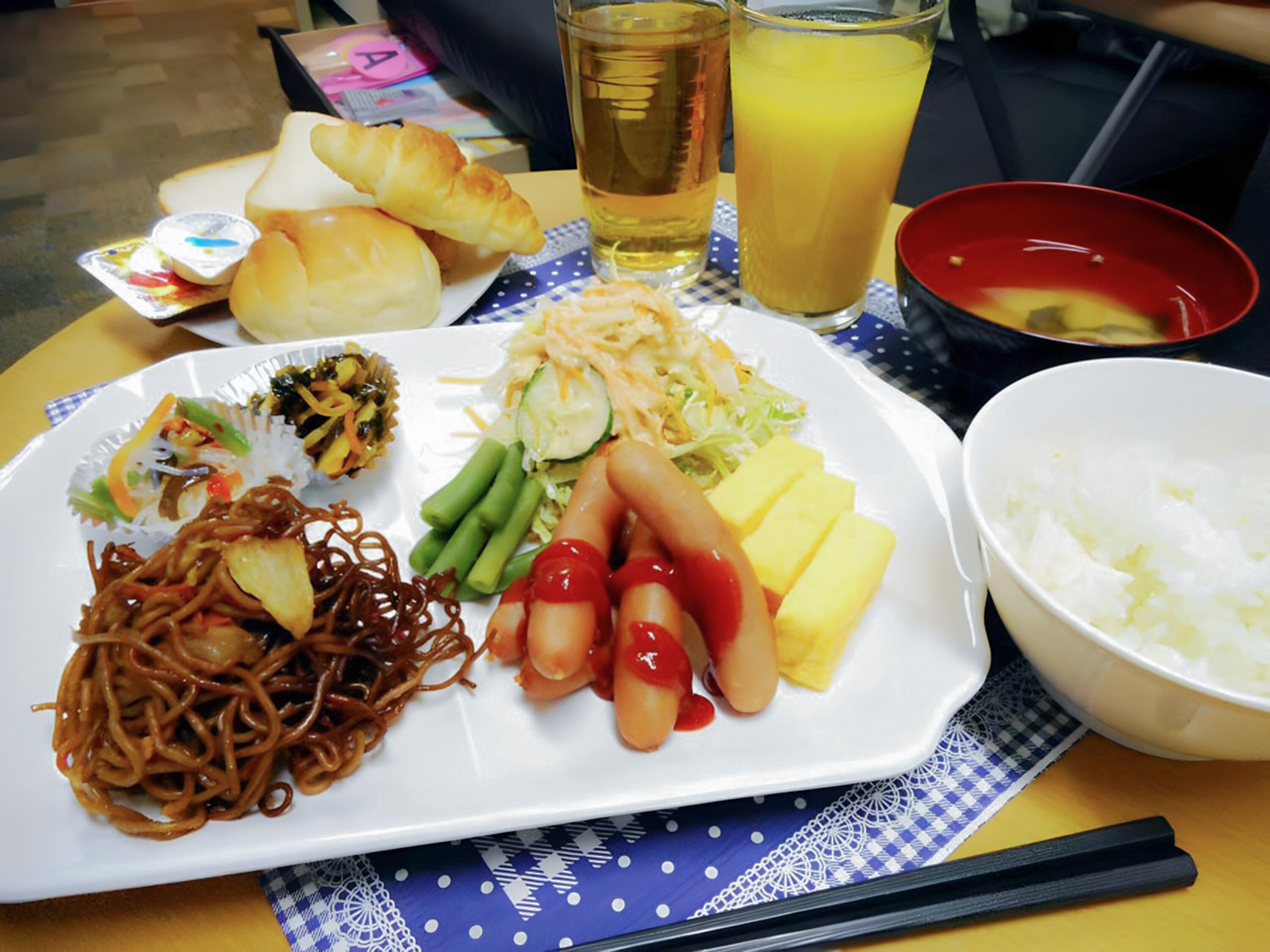 A meal with noodles, vegetables, and a bowl of rice on a table.