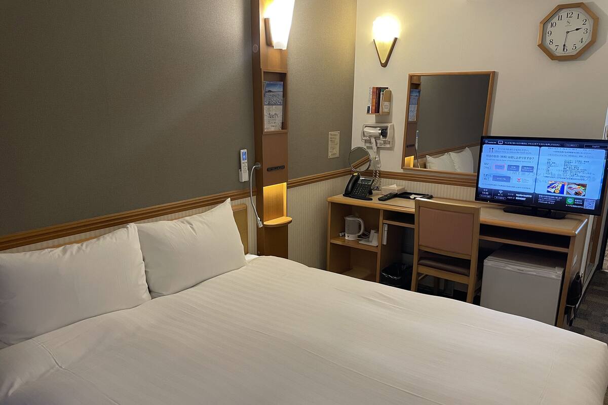 Ett hotellrum med en säng, ett skrivbord med en dator, en klocka och en spegel.