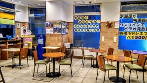A restaurant with multiple tables and chairs, a vending machine, and a blue wall with Japanese text. - Toyoko Inn Shin-osaka Chuo-guchi Shinkan (Osaka)