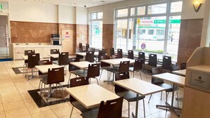 A restaurant with tables and chairs, a kitchen area, and large windows with a view of the street. - Toyoko Inn Shin Yamaguchi Station Shinkansen (Yamaguchi)