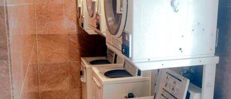 A laundry room with four front-loading washing machines and a dryer, arranged in a row against a tiled wall.