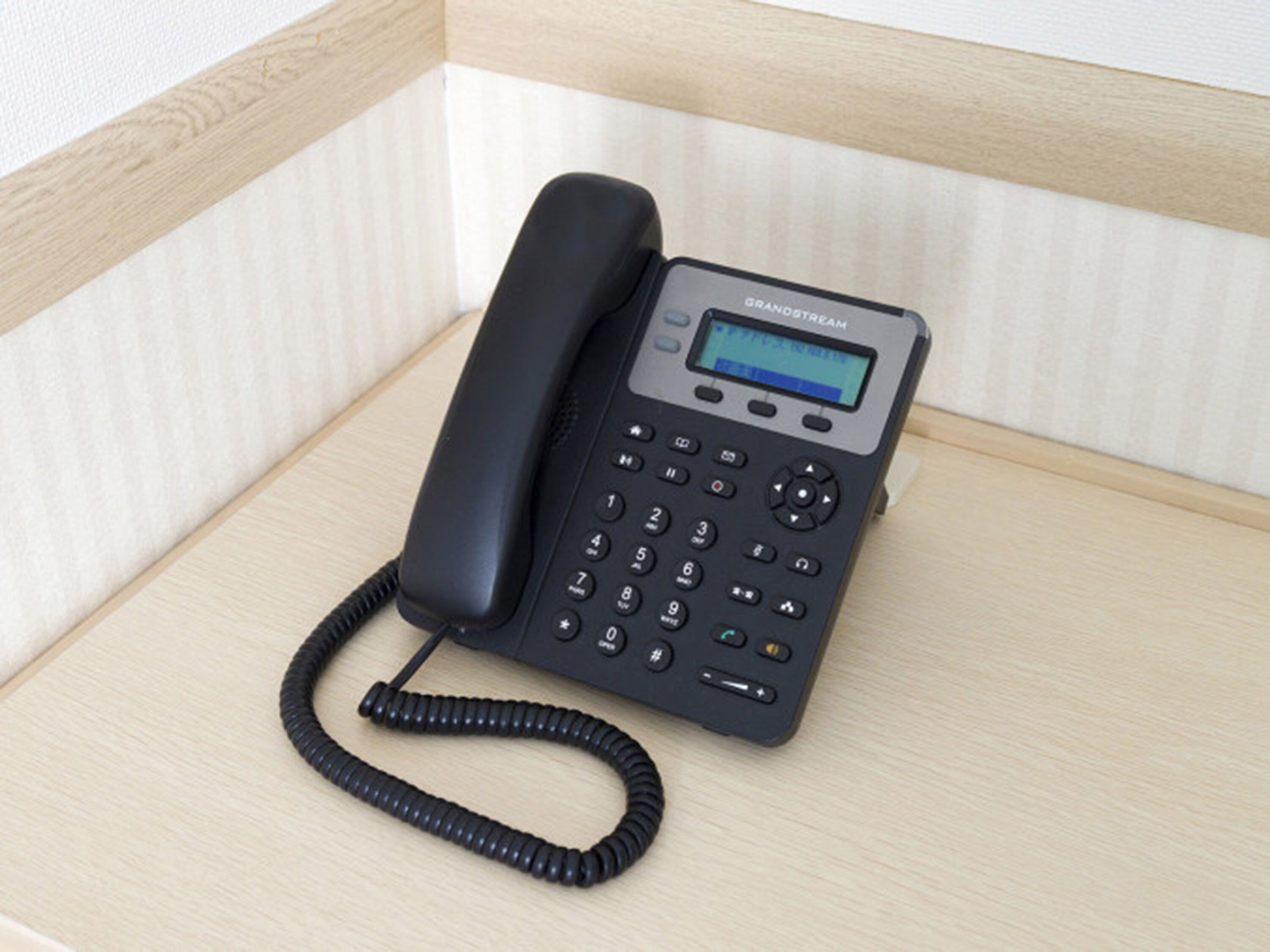 A black telephone with a keypad and a small screen, placed on a wooden surface.