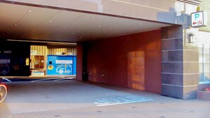 A hotel entrance with a covered parking area, a blue sign with a car and bus symbol, and a 'P IN' sign indicating parking. - Toyoko Inn Shin Yamaguchi Station Shinkansen (Yamaguchi)