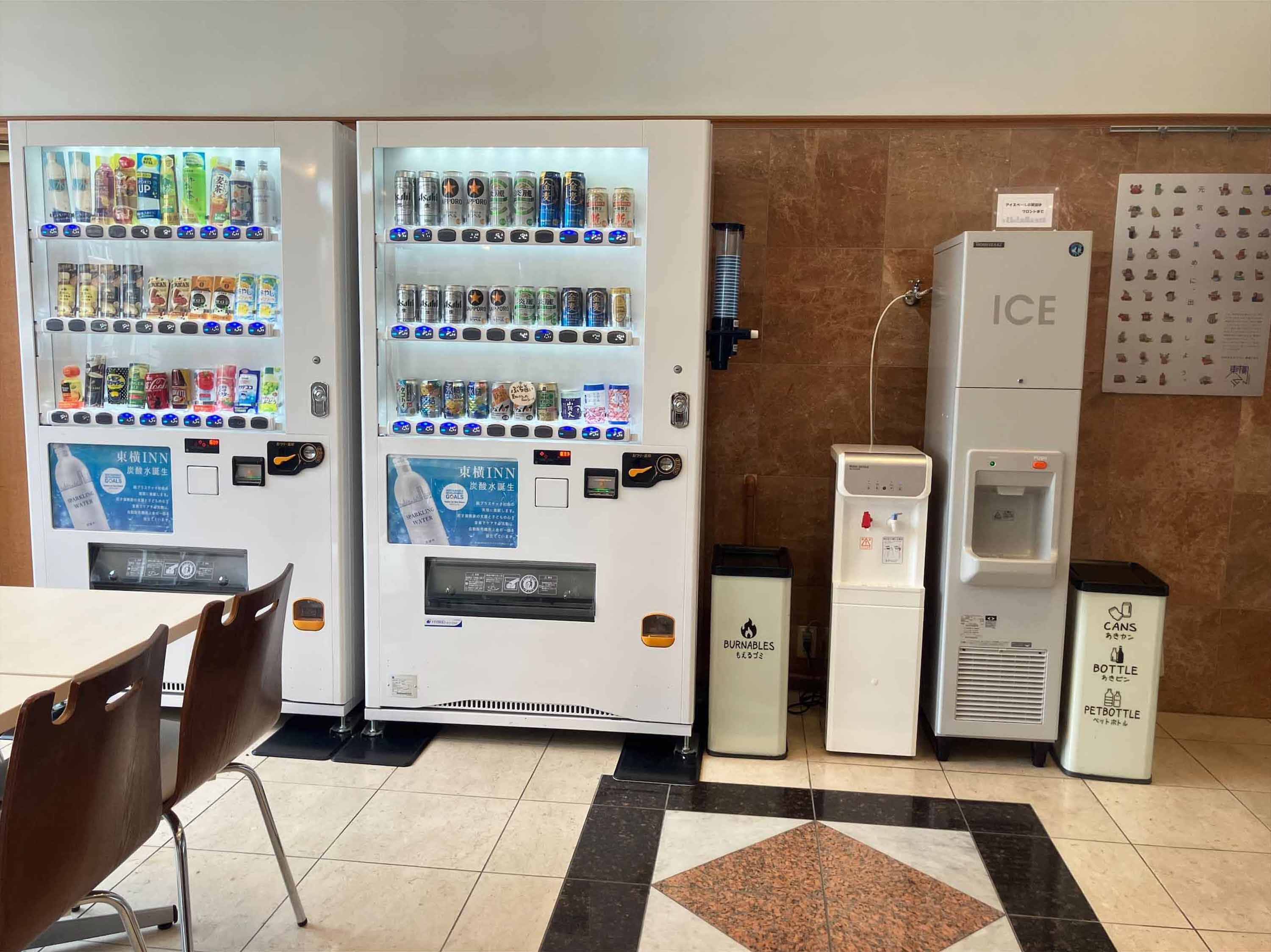 A vending machine area with various drink options, a water dispenser, and a trash bin labeled "Cans, Bottle, PETBOTTLE".