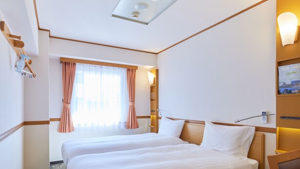 A hotel room with two beds, a window with curtains, a bedside table, and a wall-mounted lamp. - Toyoko Inn Tokyo Nihombashi Ningyocho (Tokyo)