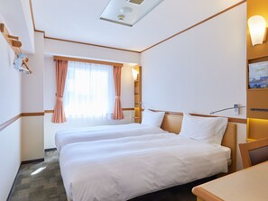 Ein Hotelzimmer mit zwei Betten, einem Fenster mit Vorhängen, einem Nachttisch und einer Wandlampe.