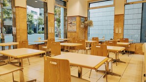A clean, modern cafe interior with wooden tables and chairs, large windows, and a tiled floor. - Toyoko Inn Tokyo Nihombashi Ningyocho (Tokyo)