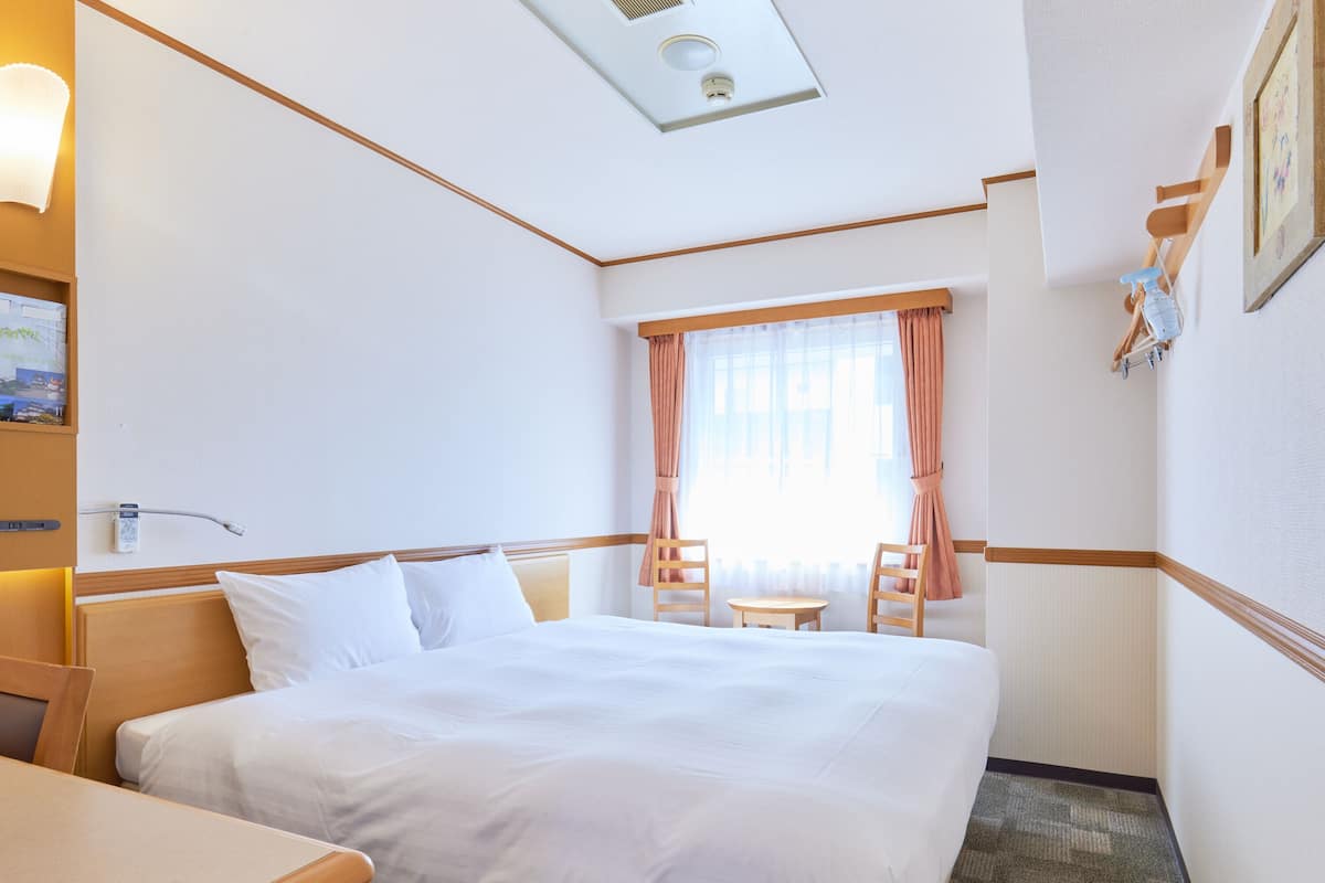 A hotel room with a bed, a desk, a chair, a small table, and a window with curtains.