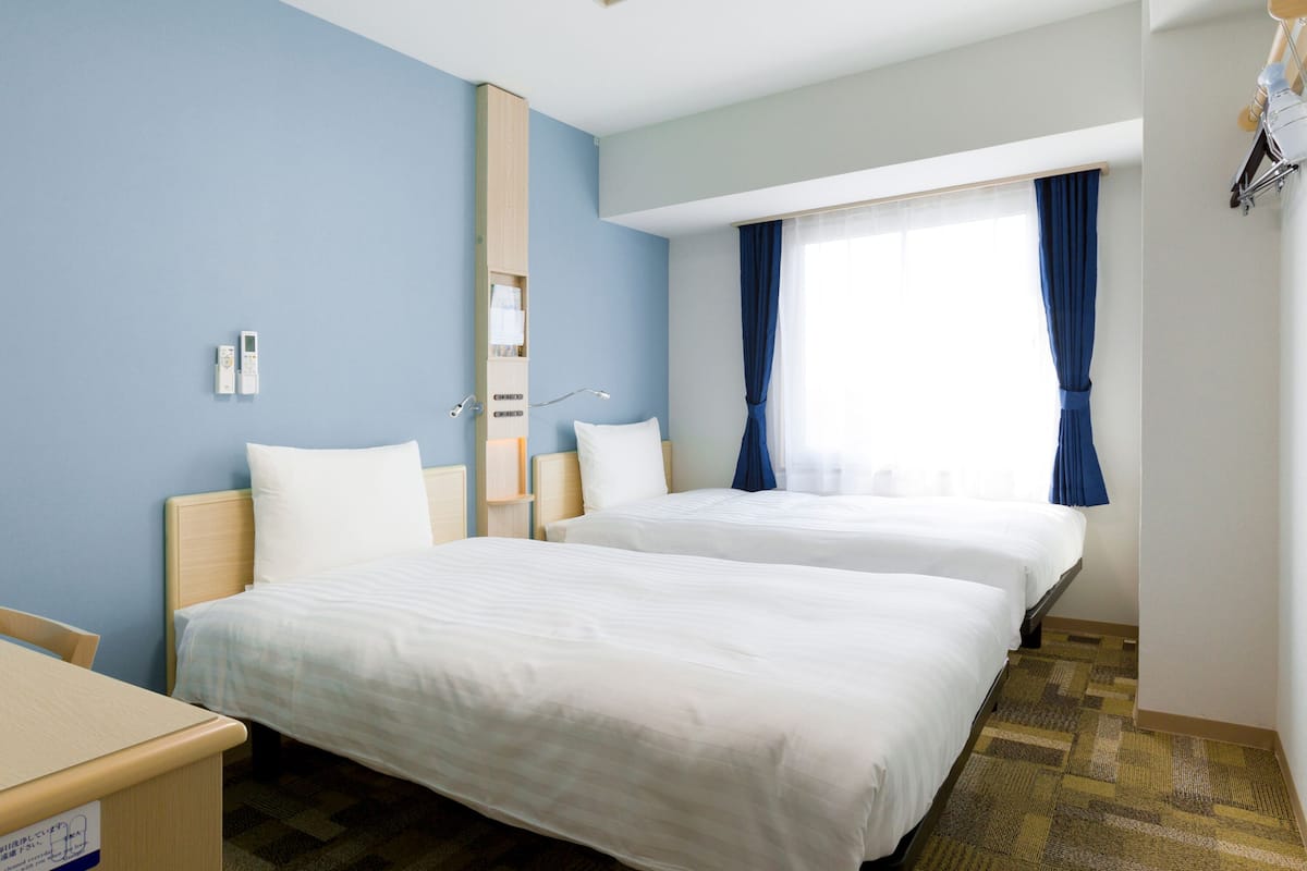 Habitación de hotel con dos camas, un escritorio, un espejo y una ventana con cortinas.