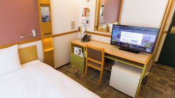 Habitación de hotel con cama, escritorio con computadora, espejo, reloj y refrigerador pequeño.