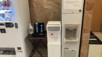 Una máquina expendedora con bebidas y aperitivos, un dispensador de agua y una pequeña mesa con una botella y vasos.