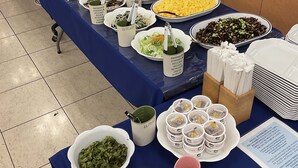 Una mesa de buffet con diversos platos, entre ellos ensaladas, arroz y un bol de verduras anaranjadas, además de varias tazas y un menú.