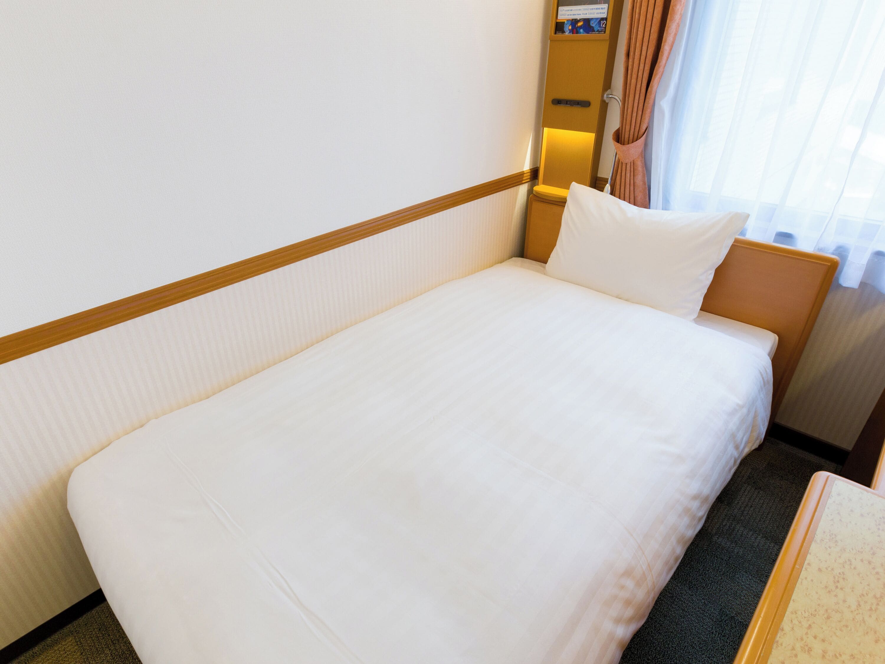 A single bed with white bedding, a wooden headboard, and a nightstand with a lamp.