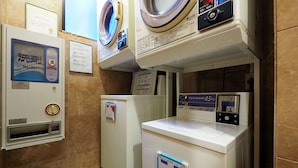 A laundry facility with multiple washing machines, a coin-operated dryer, and a trash bin.