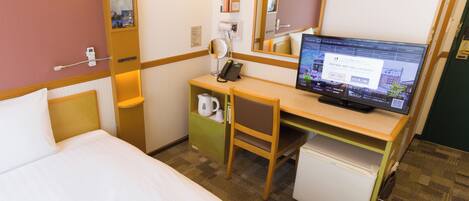 A hotel room with a bed, a desk with a computer, a mirror, a clock, and a small refrigerator.