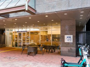 Ein Hotel mit Eingangsbereich, Glastür, Sitzgelegenheiten im Freien und abgestellten Elektrorollern.