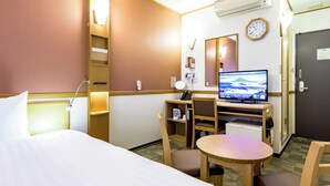 Een hotelkamer met een bed, bureau, stoel, televisie en een klok aan de muur.