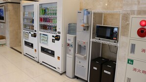 Een rij automaten met diverse drankjes en snacks, een waterkraan en een magnetron.