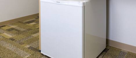 Un refrigerador blanco y compacto en un rincón de una habitación con alfombra estampada.