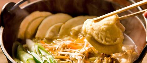 Un tazón de sopa con palillos levantando un dumpling, que contiene verduras y fideos.
