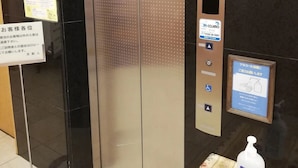 Ein Aufzug mit digitaler Anzeige der Zahl 2, einem Schild für einen 24-Stunden-Service und einem Handdesinfektionsspender.