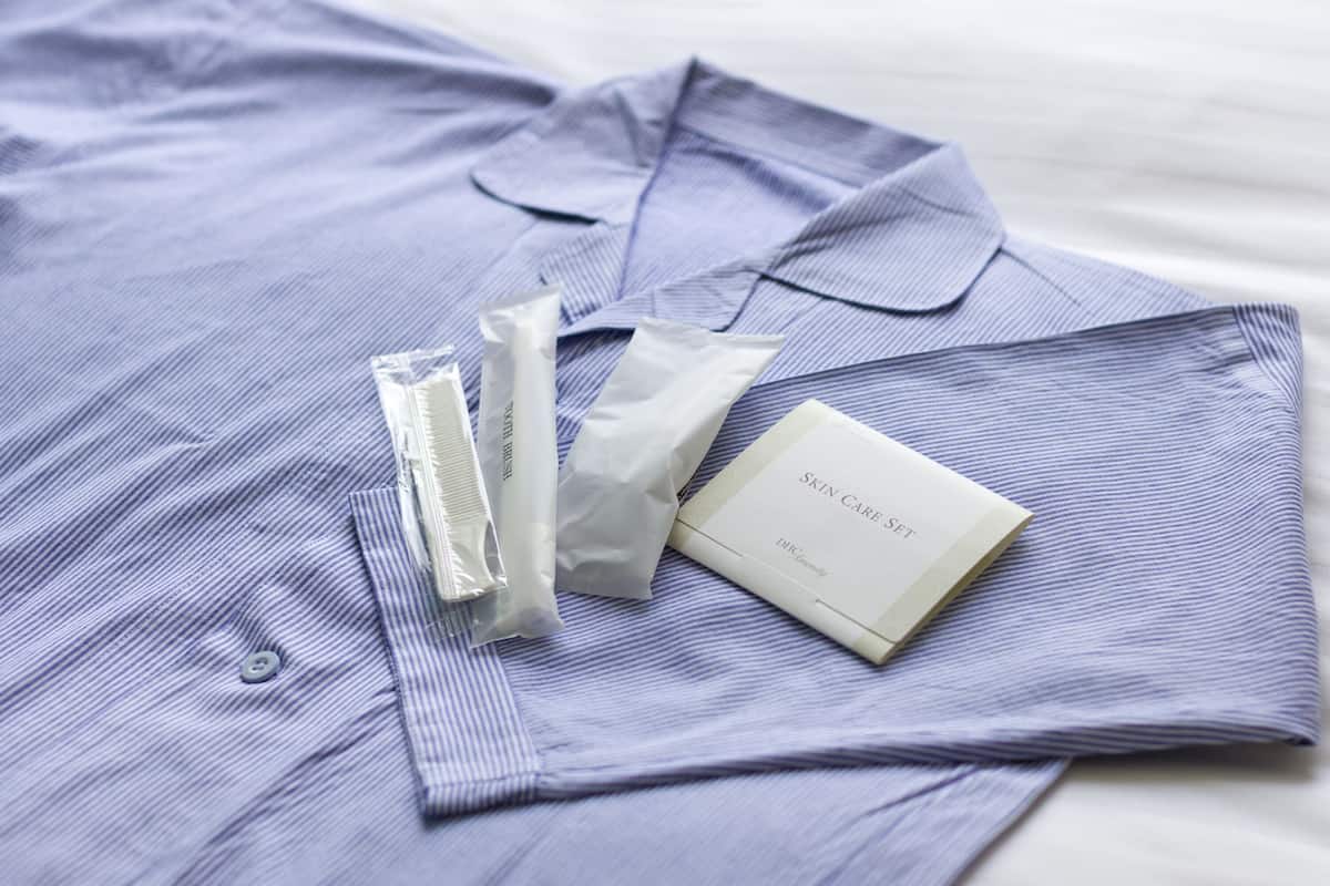 Une chemise bleue soigneusement pliée, sur laquelle est posé un ensemble de produits de soins pour la peau, comprenant un tube, un pinceau et un sachet.