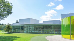 Un bâtiment moderne doté de grandes fenêtres en verre, d’une pelouse verdoyante et d’un chemin sinueux menant à l’entrée.