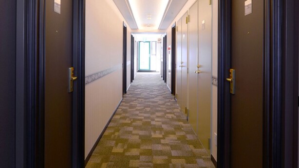 Un couloir d’hôtel avec un tapis à carreaux, des portes de chaque côté et un luminaire au plafond.