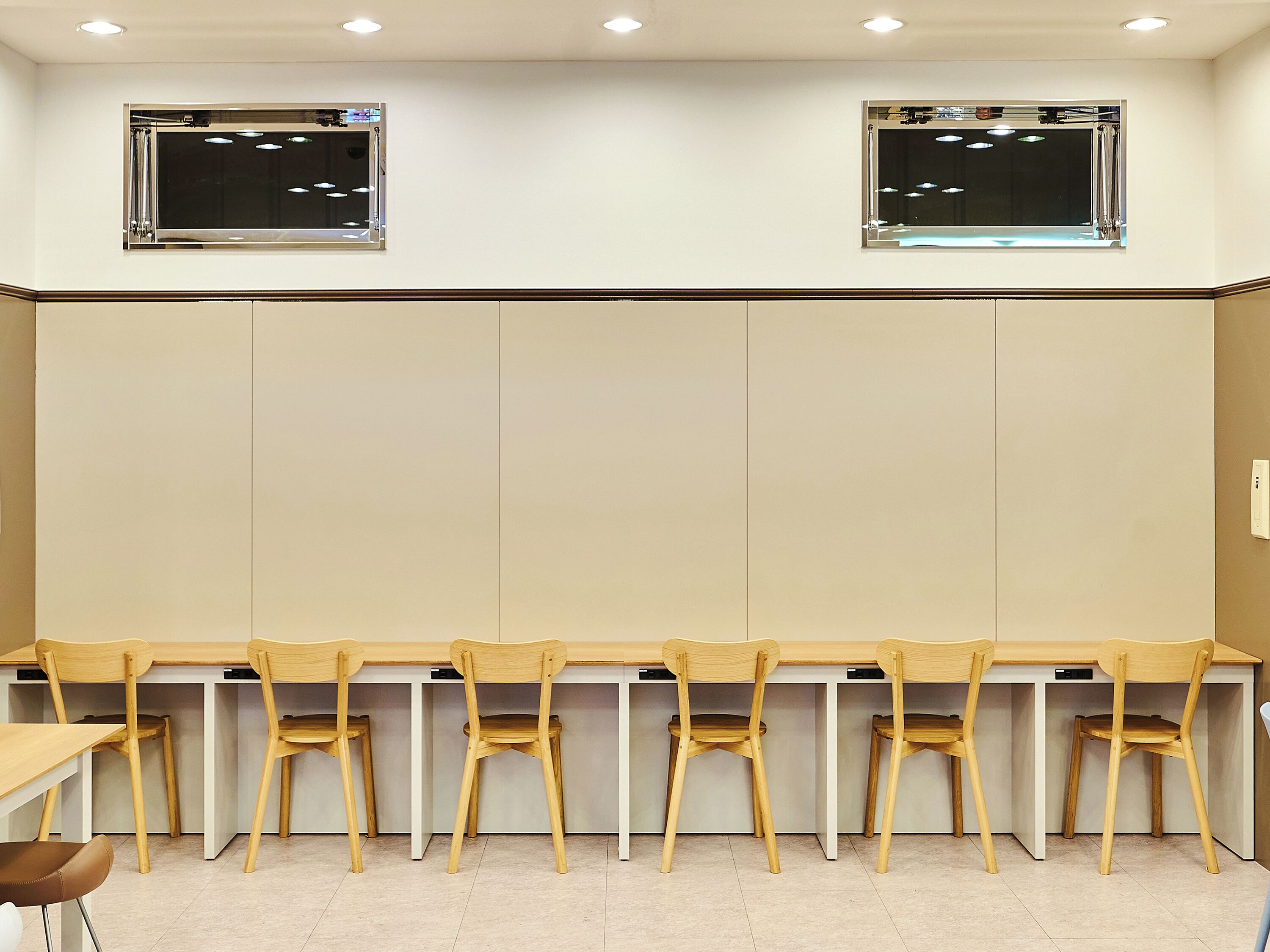 Un aula con seis escritorios y sillas de madera, paredes blancas y dos ventanas con persianas.
