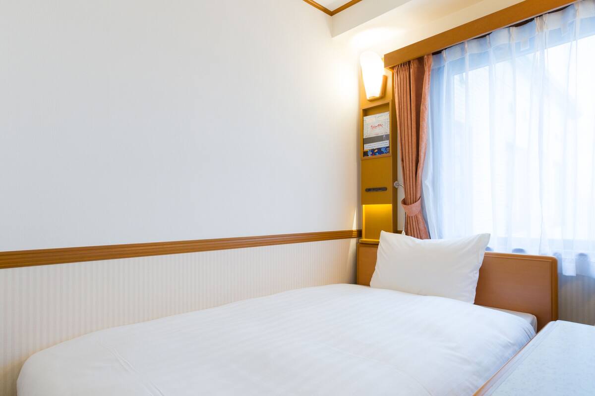 A hotel room with a large bed, a bedside table, a nightstand, a lamp, and a window with curtains.