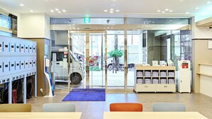 A hotel lobby with a reception desk, a vending machine, a blue locker area, and a seating area with tables and chairs. - Toyoko Inn Kawasaki Station Shiyakusho Dori (Kawasaki)