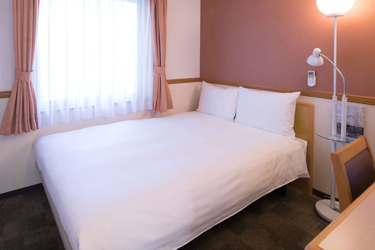 A hotel room with a large bed, a bedside table with a lamp, and a window with curtains.