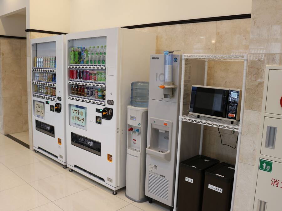 A row of vending machines with various beverages and snacks, a water dispenser, and a microwave.