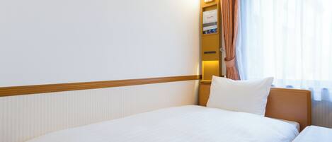 A hotel room with a large bed, a bedside table, a nightstand, a lamp, and a window with curtains.