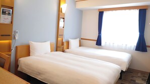 Habitación de hotel con dos camas, una mesita de noche, una lámpara de pared y una ventana con cortinas.