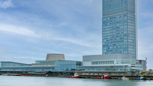 Un edificio moderno con una alta torre de vidrio y una estructura de techo plano con forma curva.